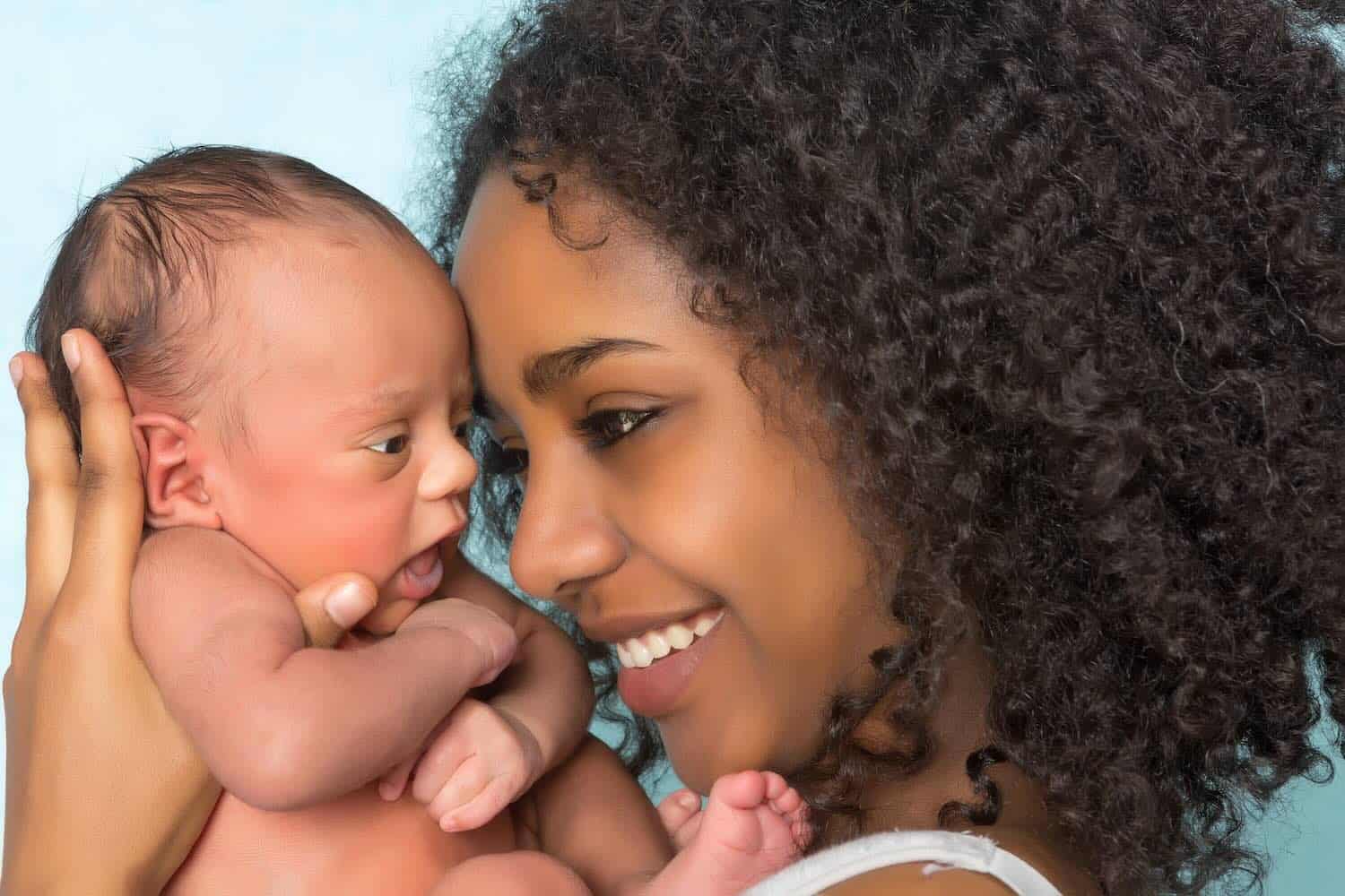 Smiling african mother and baby A woman smiles while holding a newborn baby close to her face, both appearing happy and affectionate against a light blue background.